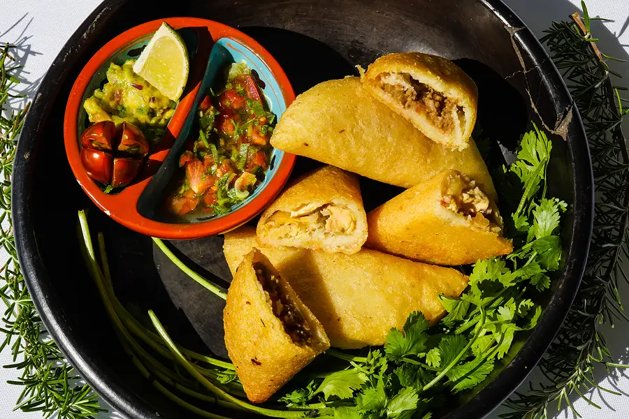 Des empanadas coupées dans une cazuela noire, avec de la coriandre et deux sauces